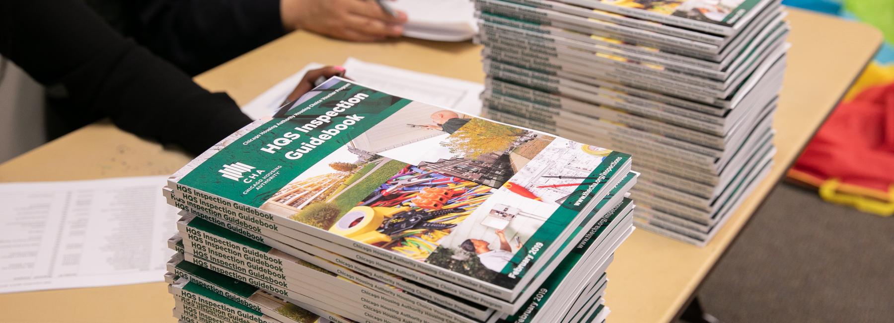A stack of HQS (Housing Quality Standards) guidebooks on a table a HCV resource fair.