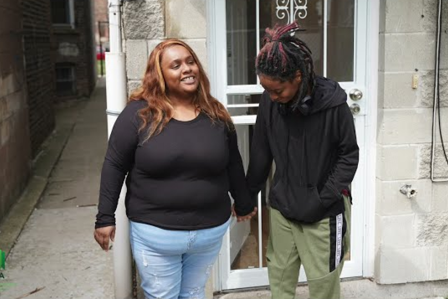 A smiling mother and child holding hands in front of a building